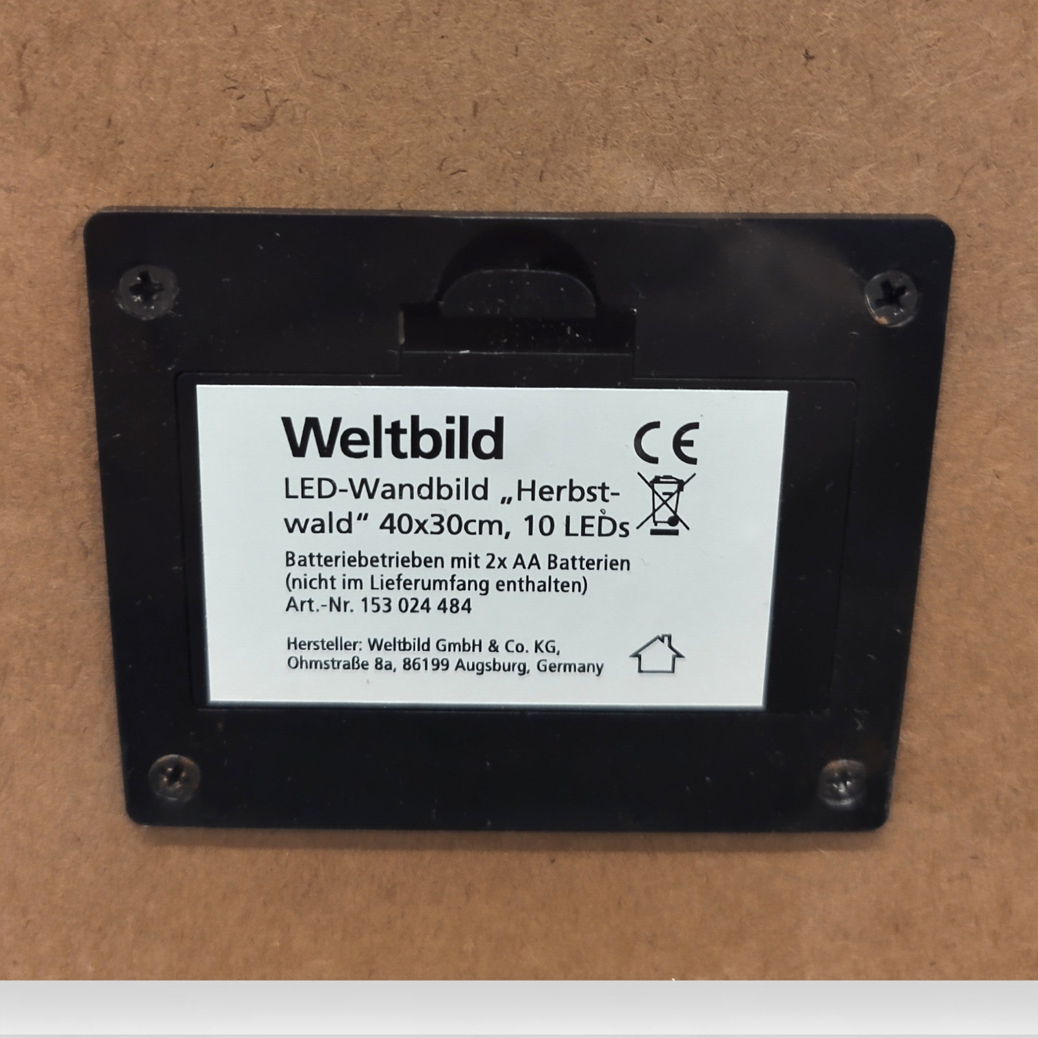 Nahaufnahme des LED-Wandbildes "Herbstwald" von Weltbild (40x30 cm, 10 LEDs, batteriebetrieben), mit Produkt-/Herstellerangaben in deutscher Sprache auf brauner Fläche.