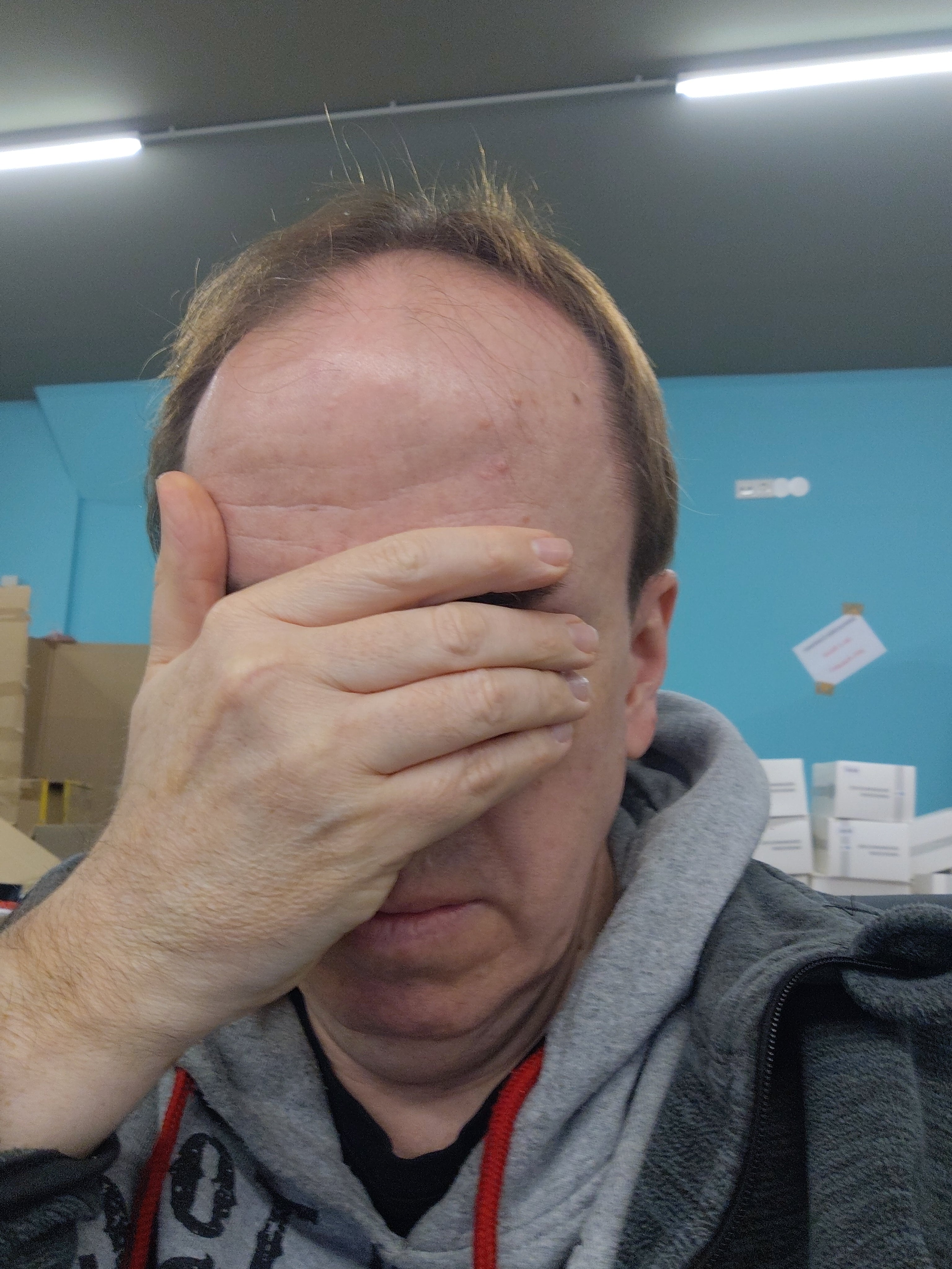 Mann hält sich die Hand vor das Gesicht im Lager mit Kartons und Paketen, Retouren-Bereich