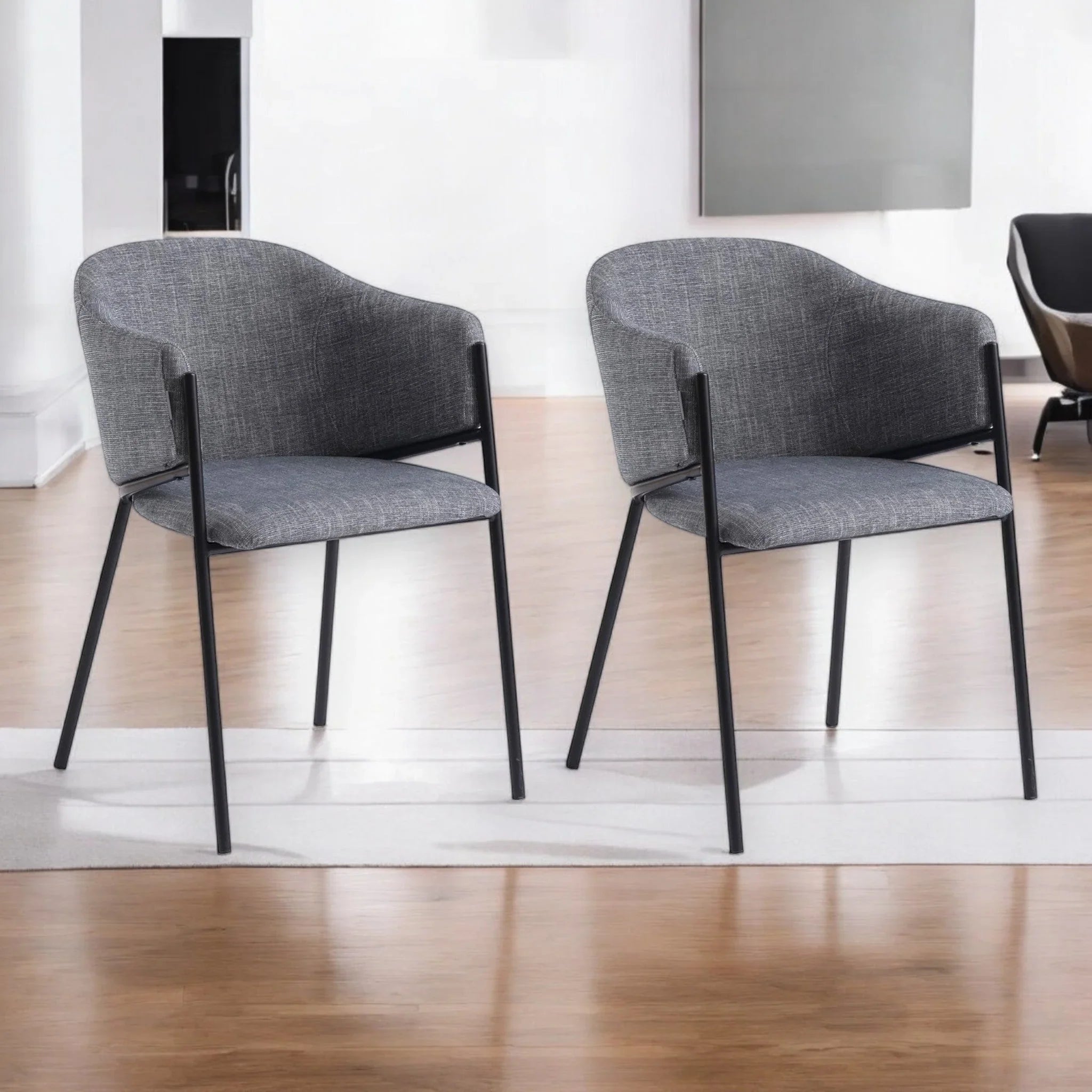 Zwei moderne graue Polstersessel mit schwarzen Metallbeinen stehen nebeneinander auf einem weißen Teppich in einem hellen, minimalistischen Raum mit Holzfußboden.