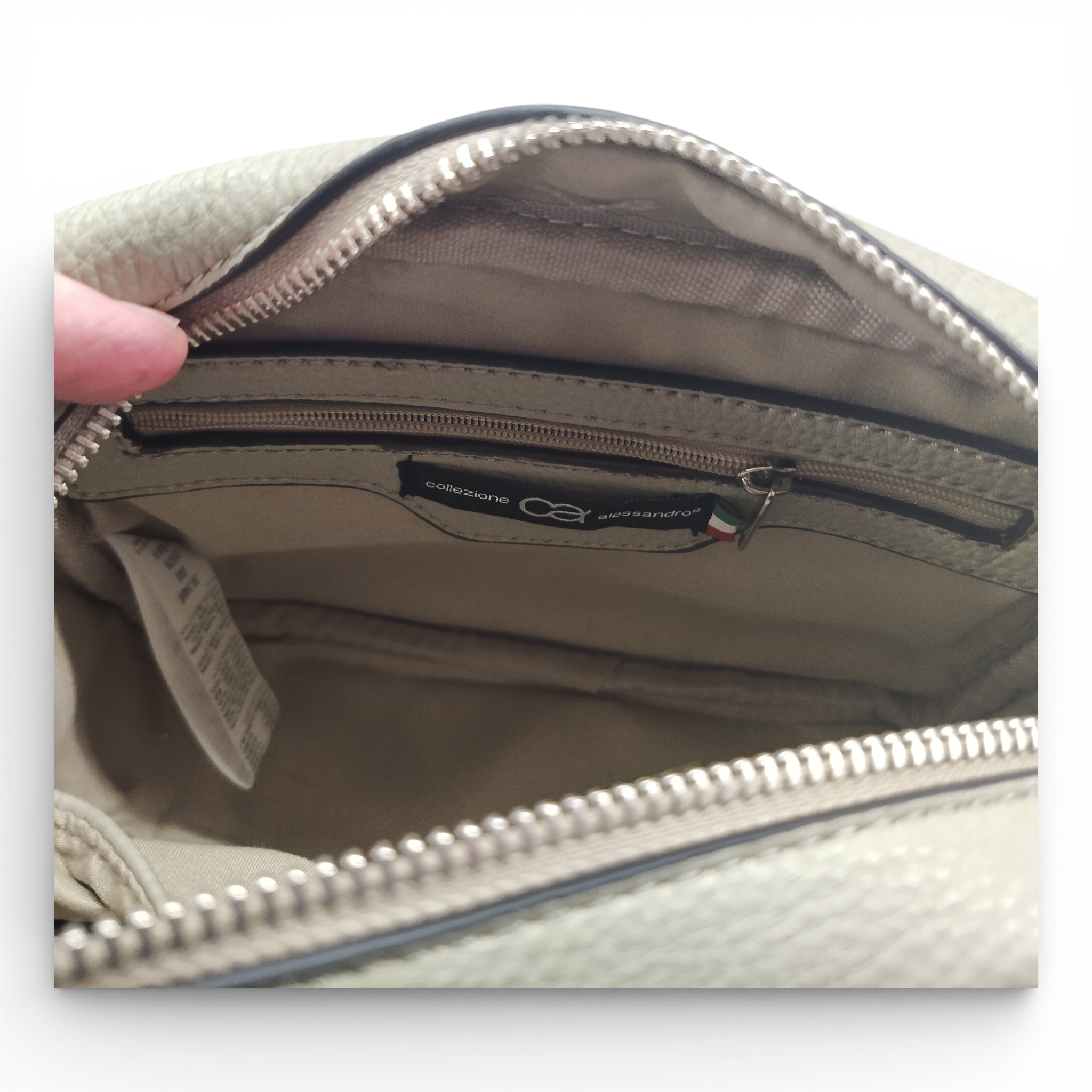 Nahaufnahme der Innenseite der beigen Schultertasche Umhängetasche von Collezione Alessandro, Made in Italy, mit einer Reißverschlusstasche, einem Stoffetikett und einem Pflegeetikett.